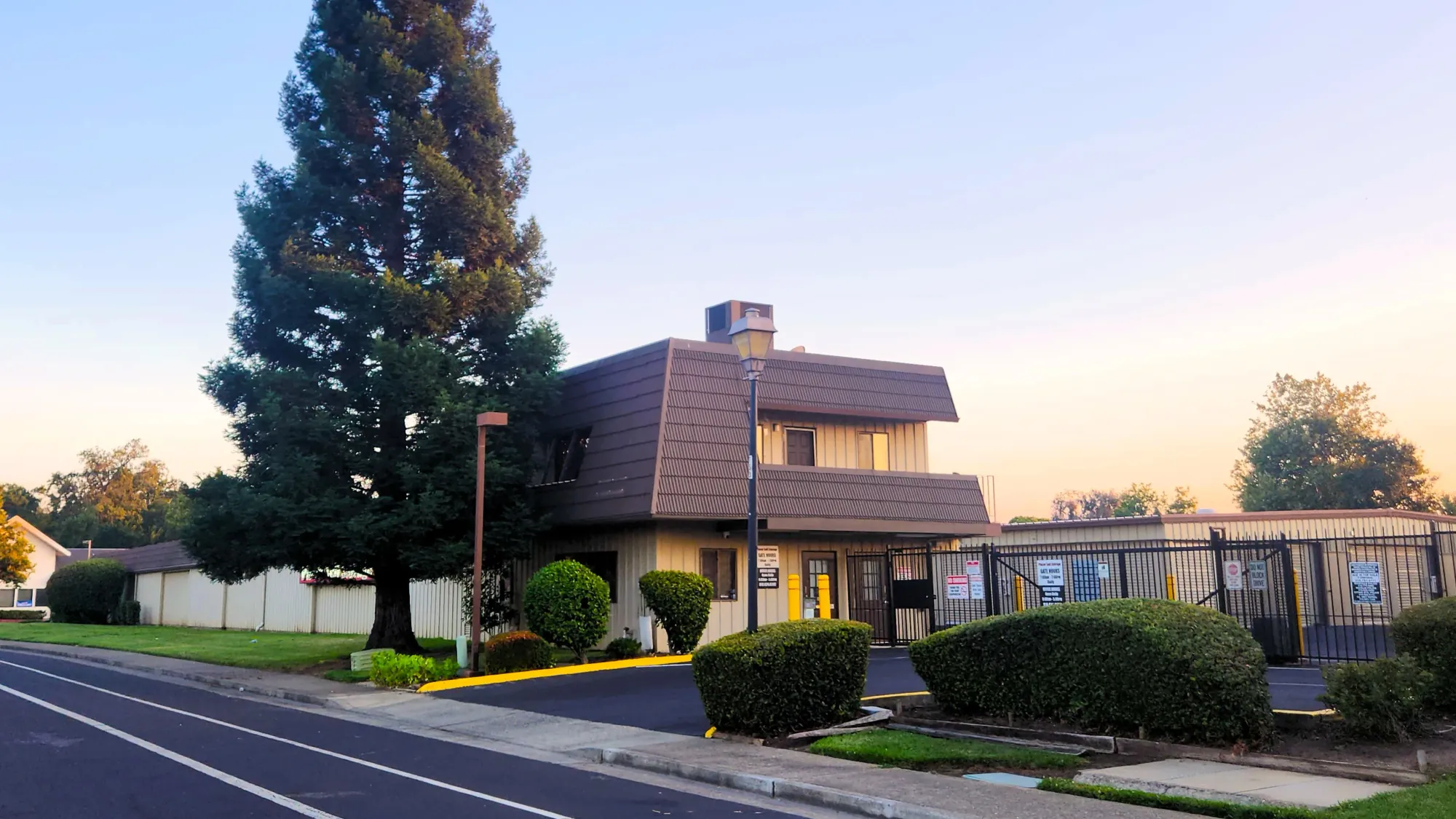 Placer Self Storage's mansard-roofed office in Rocklin, CA, at dusk beside the gated entrance